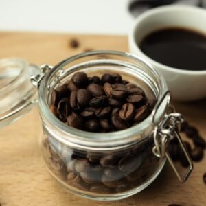 Glass jar of roasted coffee beans next to a cup of black coffee
